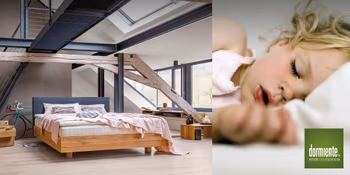 Bett mit Holzgestell im hellen Schlafzimmer mit Dachschrägen und schlafendes Kind auf dormiente-Kissen